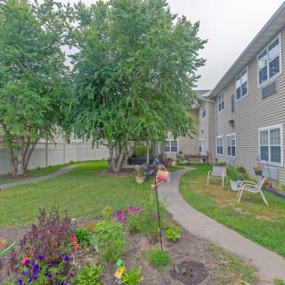 A serene garden with a pathway surrounded by greenery and flowers, adjacent to residential buildings.