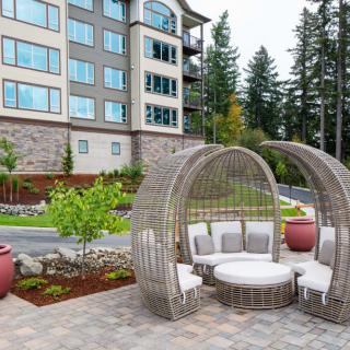 A modern outdoor seating area with stylish furniture in front of an apartment building, set amidst landscaped greenery.