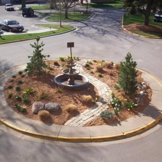 A landscaped roundabout featuring a variety of plants, trees, and a central rock garden.