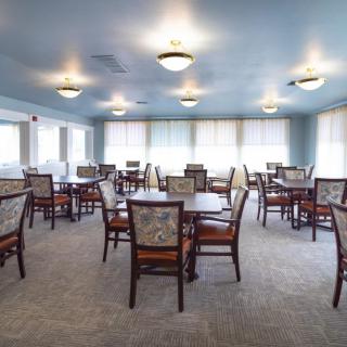 A spacious dining room with multiple tables and chairs, well-lit by ceiling lights.