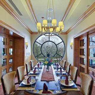 An elegantly set dining room with a large circular window and a chandelier overhead.