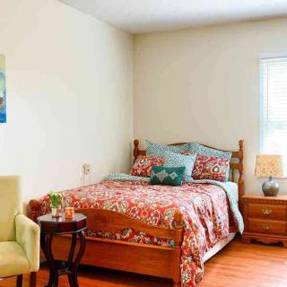 A cozy bedroom with a floral bedspread, wooden furniture, and a window letting in natural light.