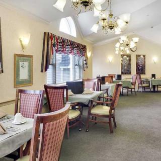 A spacious dining room with neatly arranged tables and chairs, illuminated by elegant chandeliers.