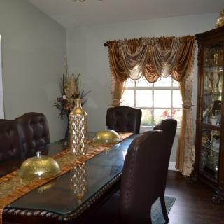 A stylish dining room with elegant furniture and decorative accents, featuring a large window with ornate curtains.