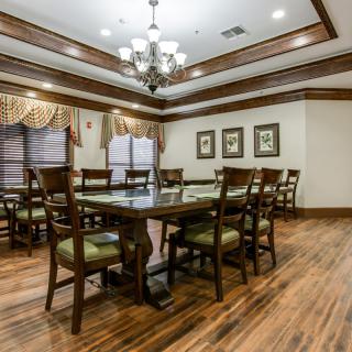 A spacious dining room with traditional decor, featuring a large wooden table and chairs, elegant chandelier, and wood flooring.