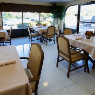 A cozy restaurant interior with neatly arranged tables and chairs, illuminated by natural daylight coming through large windows.