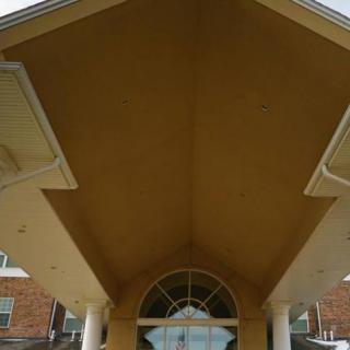 The exterior entrance of a building featuring a peaked roof and supporting columns.