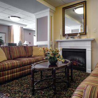 A cozy living room with striped sofas arranged around a wooden coffee table, featuring a fireplace topped with a mirror.