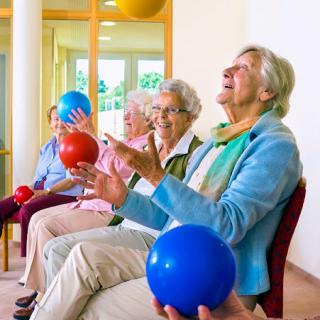 A group of seniors engaging in a fun indoor exercise activity with colorful balls.