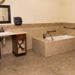 A spacious bathroom featuring a large bathtub with surrounding tiles, a sink with cabinet storage, and a wall-mounted mirror.