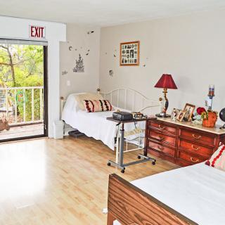 A nursing home bedroom with two beds, a dresser, and a balcony view.