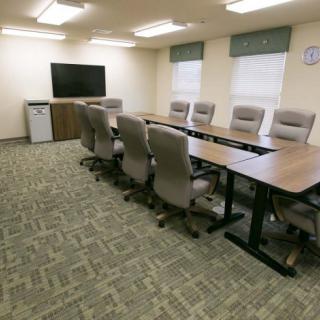 A well-lit conference room with a long table, several chairs, and a TV screen.