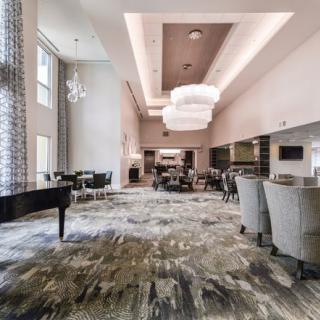 A modern lounge area featuring a grand piano, elegant chandeliers, and comfortable seating.