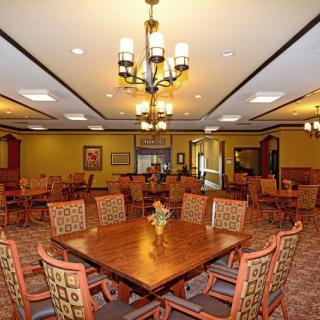 A spacious dining area with neatly arranged tables and chairs, illuminated by a central chandelier.