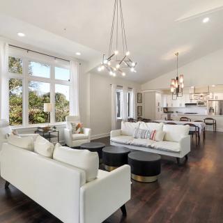 A spacious and elegantly decorated living area with white furnishings, modern chandeliers, and ample natural light.