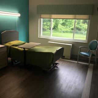 A clean and serene patient room with a bed, chair, and large window providing natural light.