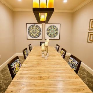 A modern dining room with a long wooden table, surrounded by chairs and decorated with candles and artwork on the walls.