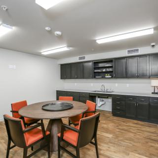 A modern kitchen and dining area featuring a round table with orange chairs, wood flooring, and sleek cabinetry.