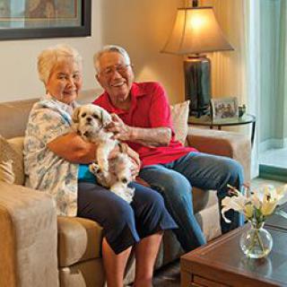 An elderly couple sitting on a sofa with their dog in a cozy living room.