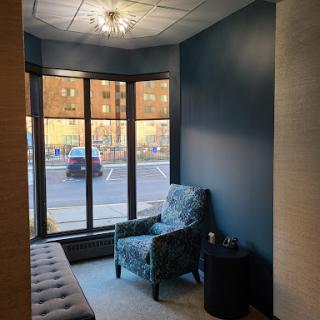 A cozy waiting area with contemporary blue walls and a comfortable armchair, illuminated by natural light from large windows.