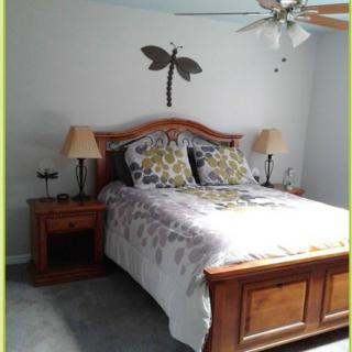 A cozy bedroom featuring a wooden bed with floral bedding, flanked by nightstands and a decorative dragonfly wall piece.