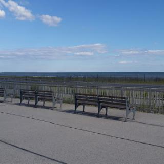 A serene view of benches lined up along a walkway with an expansive ocean view under a clear blue sky.