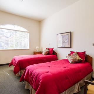 A cozy bedroom with two twin beds featuring bright red bedding, a window allowing natural light, and simple decor.