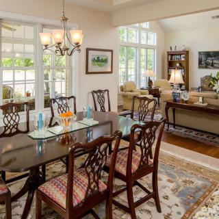A spacious dining and living area featuring a glass-top table with wooden chairs, large windows, and a cozy seating arrangement.