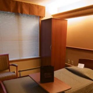 A hospital room with a bed, chair, and cabinet near a window.