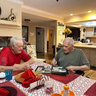 Two elderly men looking through a photo album at a kitchen table.