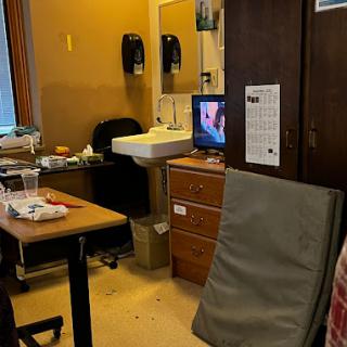 A view of a cluttered room featuring a desk, chair, and television.