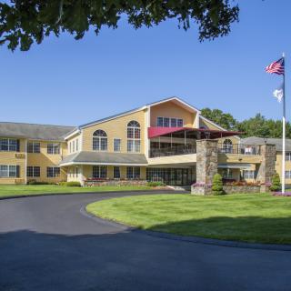 A sunny day view of a residential building with flags in front, surrounded by a well-maintained lawn and driveway.