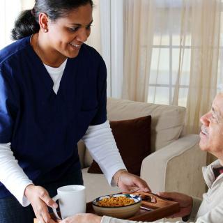 A caregiver providing a meal to an elderly person at home.