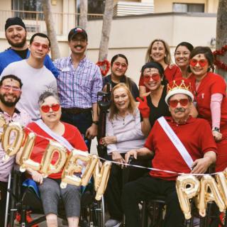 A joyful group gathers outdoors to celebrate with balloons and festive sunglasses.