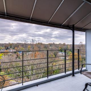 A spacious balcony with a metal railing overlooks a scenic landscape filled with autumn foliage under a cloudy sky.