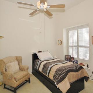 A minimalist bedroom with a single bed, armchair, and ceiling fan.