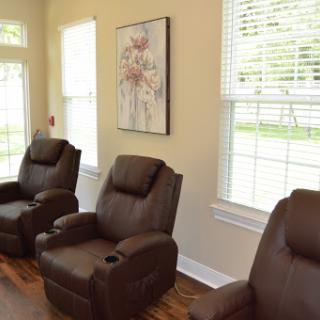 A cozy living area featuring comfortable brown recliners and a serene piece of artwork, illuminated by natural light from the large windows.