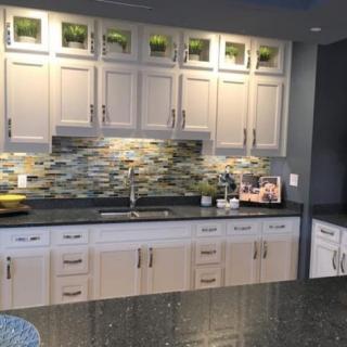 A modern kitchen featuring white cabinets, a dark countertop, and a decorative backsplash.