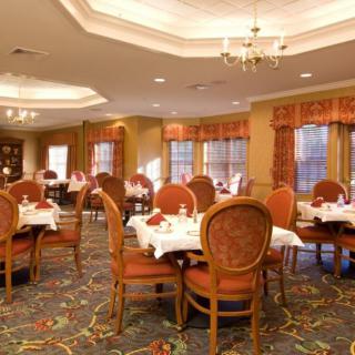 An elegant dining room with neatly arranged tables and chairs, featuring a chandelier and carpeted flooring.