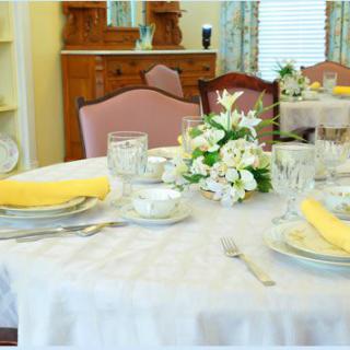 A dining table elegantly set with plates, glasses, yellow napkins, and a floral centerpiece.