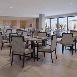 A modern, empty dining area with neatly arranged tables and chairs, featuring large windows.