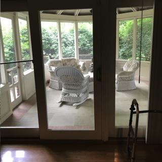 A cozy porch area with wicker furniture and large windows overlooking greenery.
