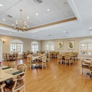 A spacious dining room with wooden flooring, elegant chandeliers, and neatly arranged tables and chairs.