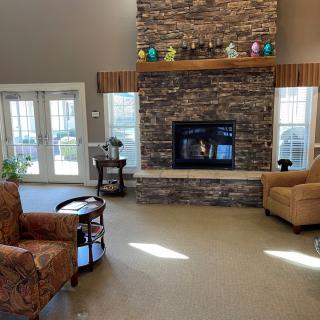 A cozy living room featuring a stone fireplace, surrounded by comfortable armchairs and large windows.