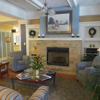 A cozy living room with a central fireplace, surrounded by comfortable seating and decorated with paintings and plants.