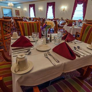 A formal dining room with elegantly set tables and vibrant red napkins.