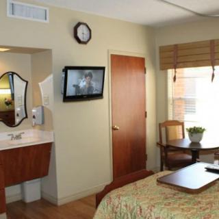 A cozy hotel room featuring a bed, wall-mounted TV, sink area, and a small table by the window.