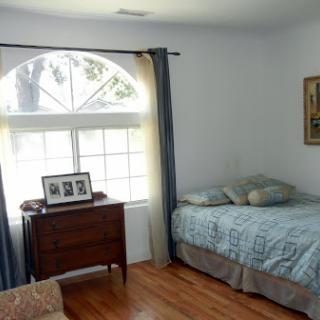 A cozy bedroom featuring a comfortable bed, wooden furniture, and ample natural light from the large window.
