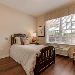 A cozy bedroom with a single bed, wooden furniture, and a large window.