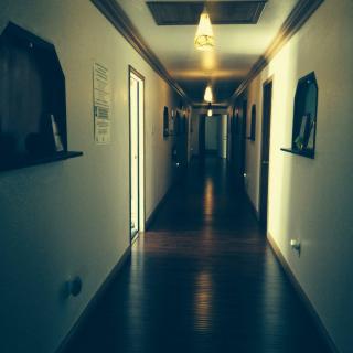 A dimly lit hallway with wooden flooring and wall-mounted lights.